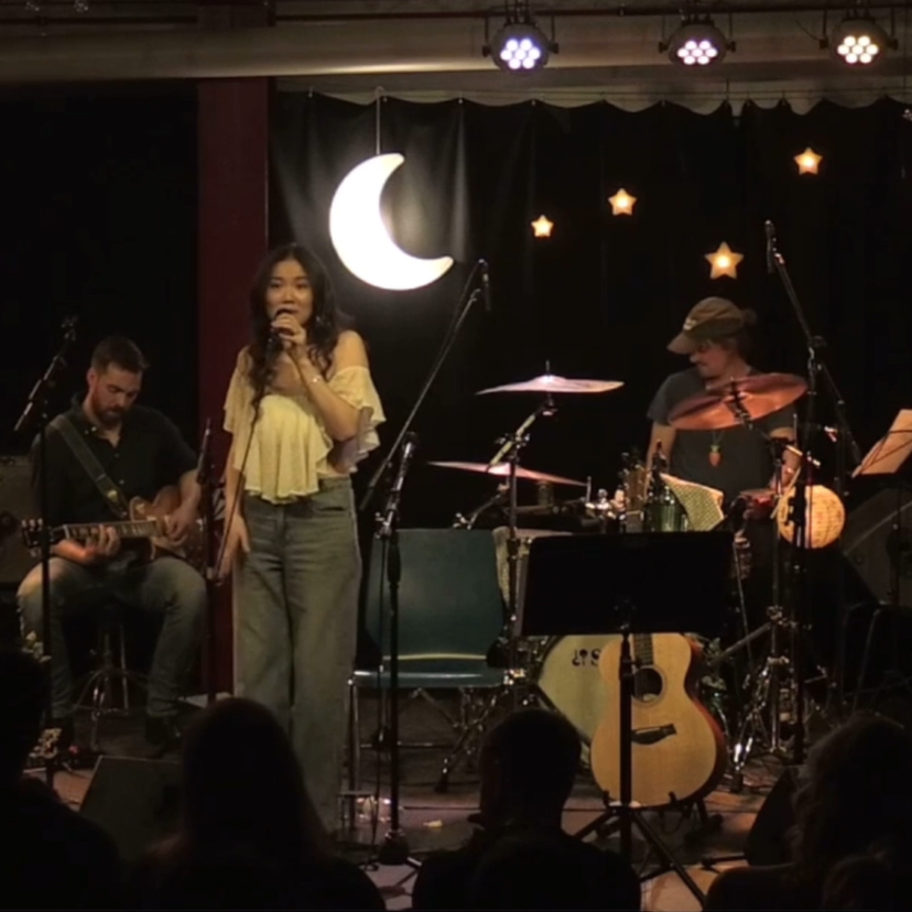 Xiao singing with a guitarist and drummer beneath moon and star stage lights