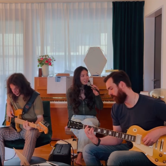 Xiao singing with two guitarists in an intimate acoustic session